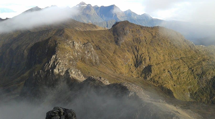 Rugged mountain terrain with steep ridges and rocky outcrops shrouded in low-hanging clouds and mist, depicting the alpine environment of Mount Wilhelm.