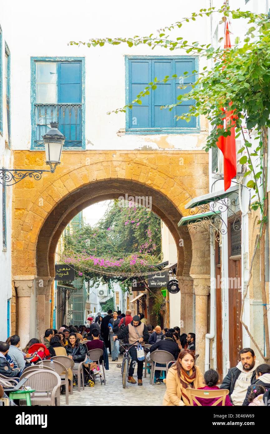 Street view of a market area in Sidi Ben Arous, Tunisia, featuring traditional buildings and outdoor cafes