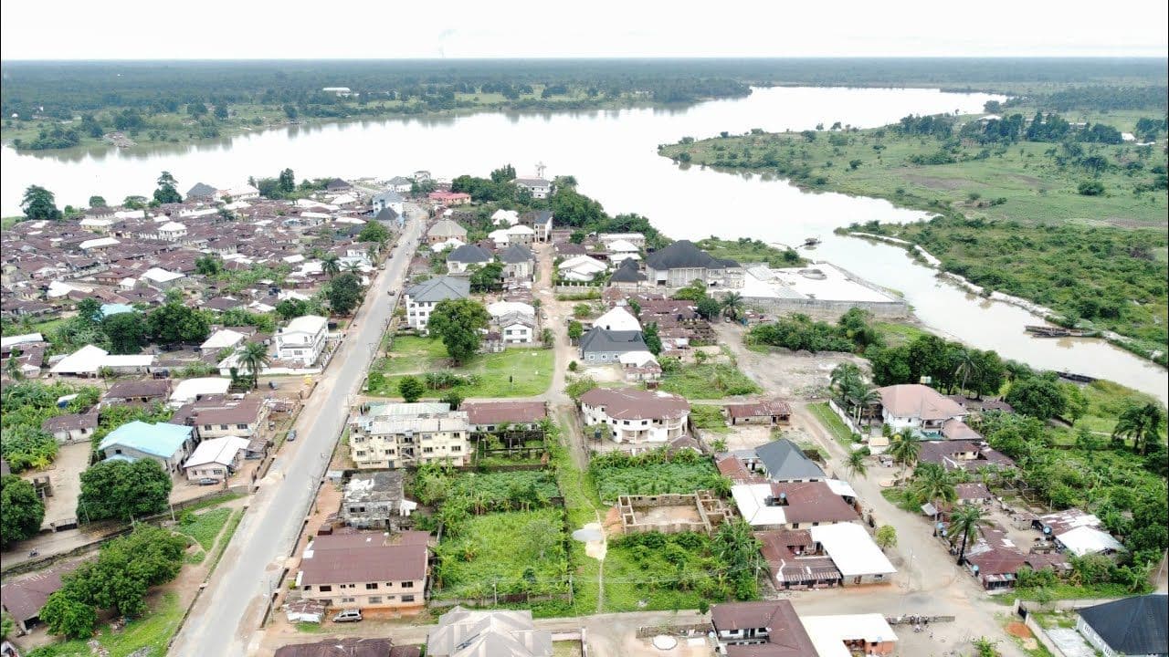 Aerial view of a town situated beside a large lake, featuring a prominent paved road winding through residential buildings and green vegetation.