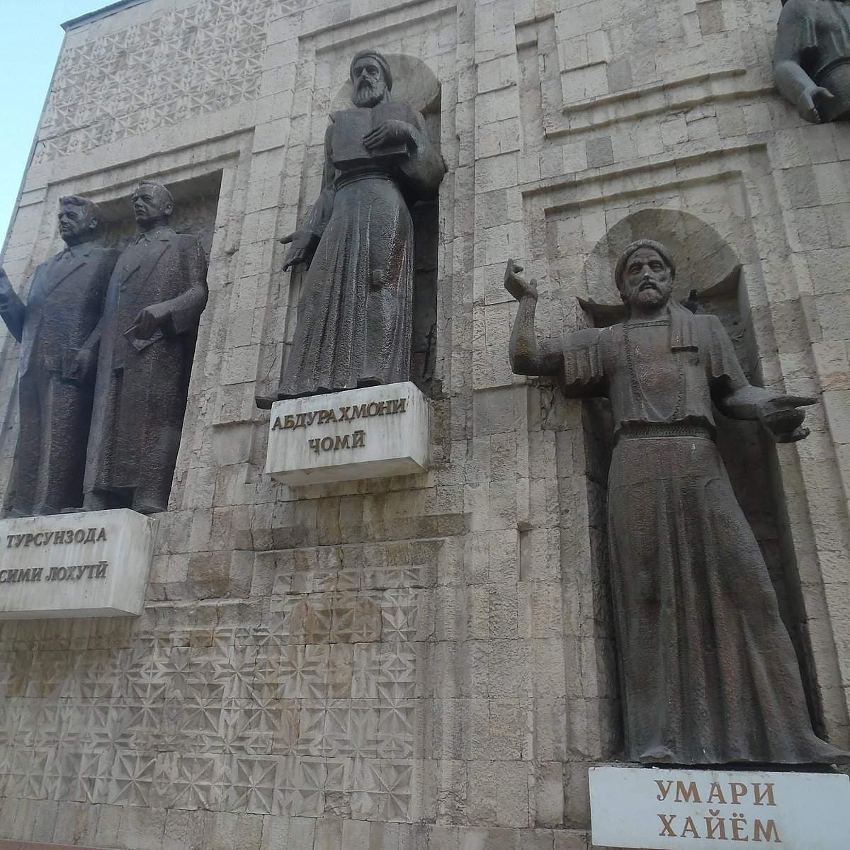 Bronze statues of historical figures, including poet Mirzo Tursunzoda, mounted on a stone building facade with Cyrillic name plaques.