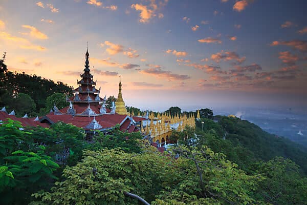 Sunset view from Mandalay Hill featuring traditional pagodas and golden stupas overlooking the distant city and Irrawaddy River.