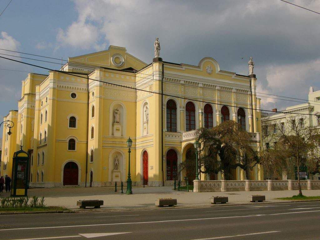 Exterior view of the yellow Csokonai National Theatre in Debrecen, featuring classical architecture, statues, and a street foreground.