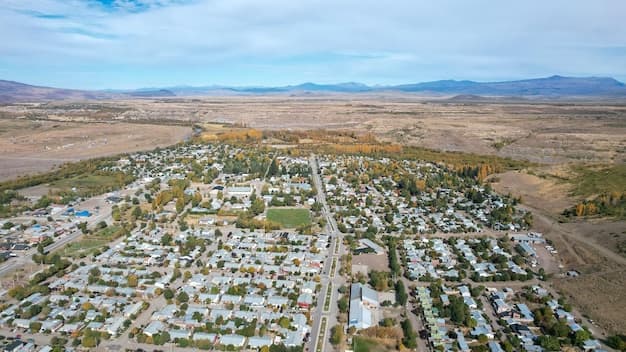 Aerial view of a residential town nestled in a dry valley with distant mountains and autumn-colored trees.