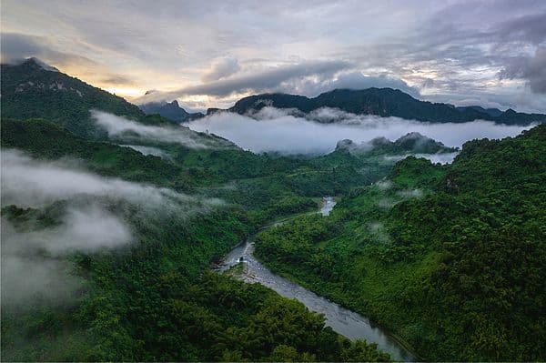 Aerial view of lush green mountains and valleys in Namosi, with a winding river and low-hanging mist drifting through the landscape.