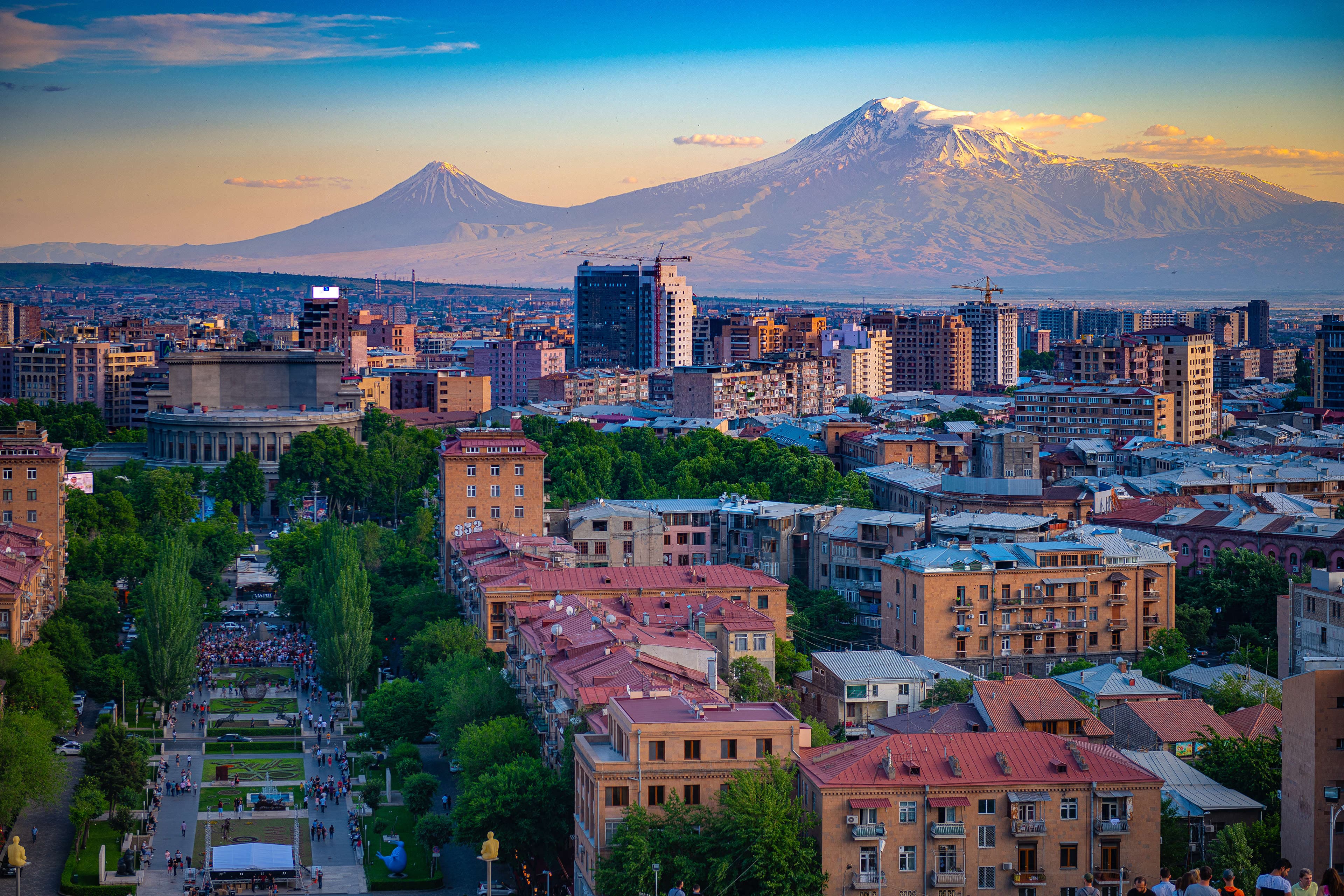Panoramic view of Yerevan cityscape with Mount Ararat in the background, featuring urban architecture and a tree-lined pedestrian boulevard.