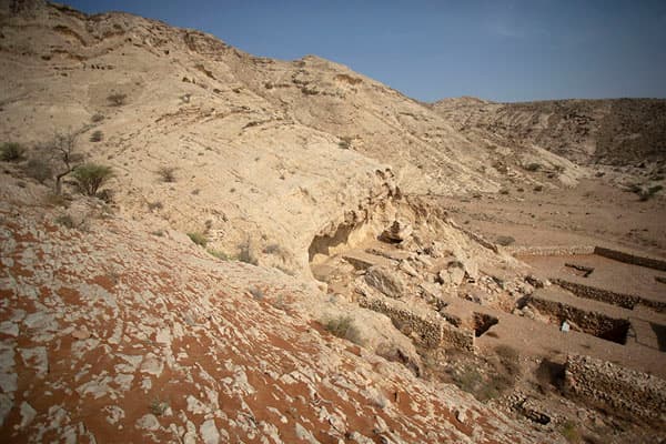 Arid desert landscape featuring ancient stone ruins and cave dwellings carved into a rocky hillside at Mleiha Archaeological Centre.