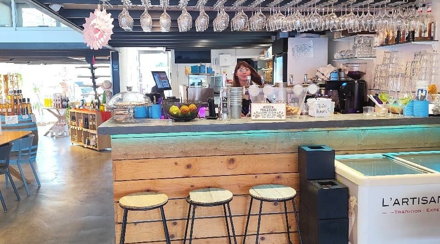 Interior view of a café bar counter in Hyères featuring wooden paneling, hanging glassware, and a barista behind the service area.