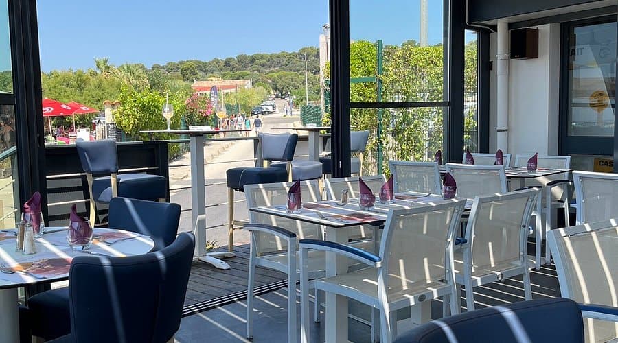 Sunlit café terrace with white and blue chairs overlooking a street and greenery in Hyères.