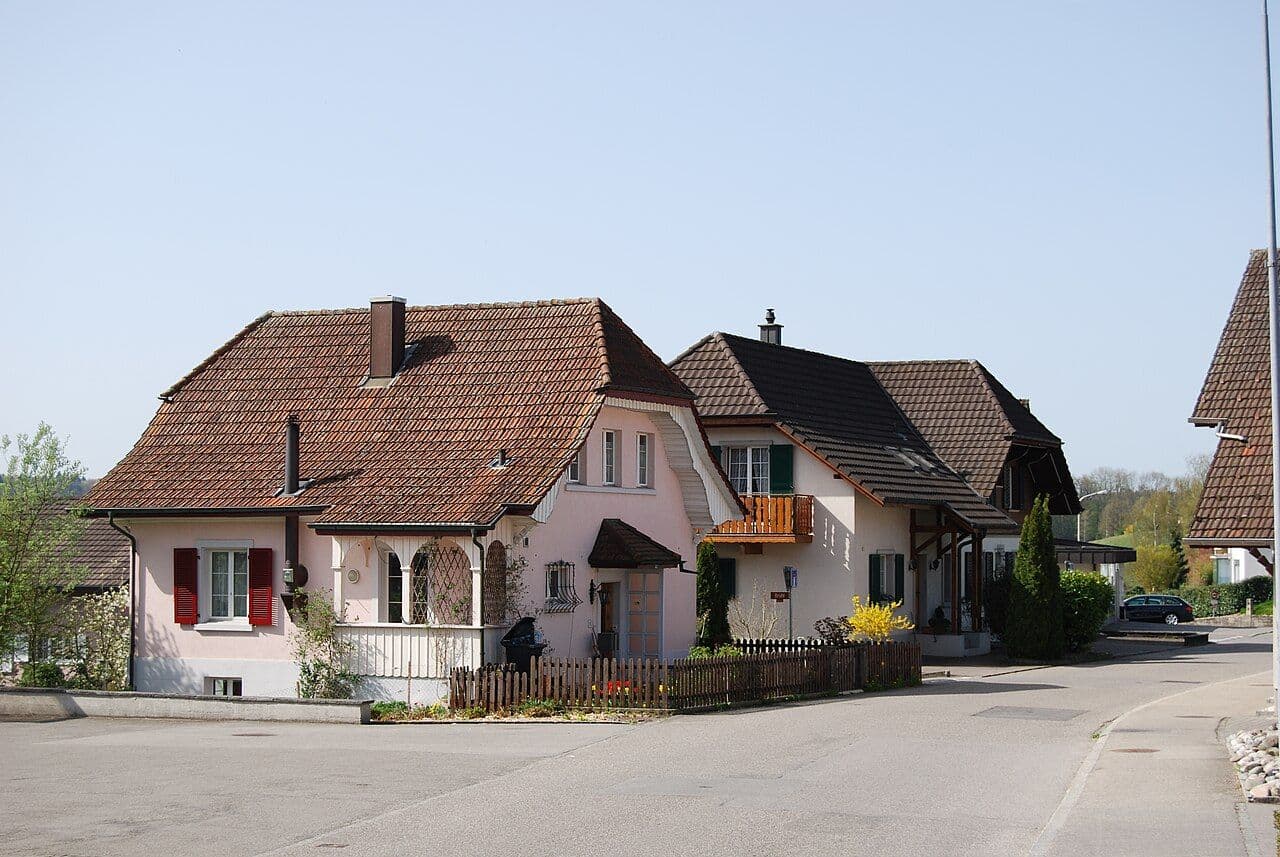 Exterior view of residential village buildings with tiled roofs, fences, and a paved street in Wolfwil, Canton Solothurn.