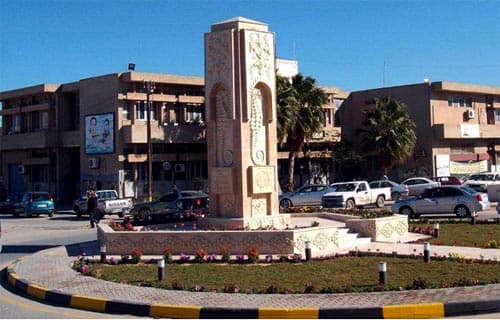Tall ornate stone memorial monument in a landscaped roundabout in Zuwārah under blue sky