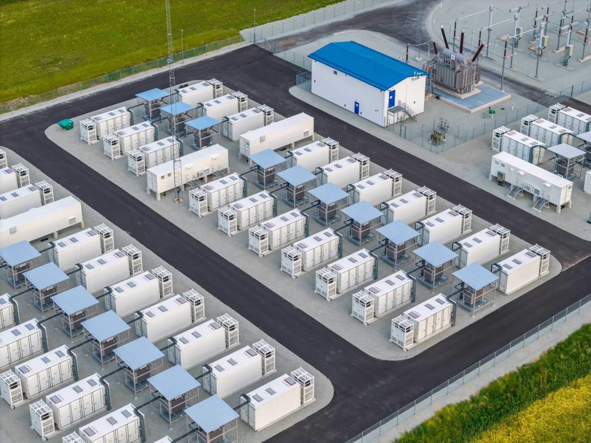 Aerial view of the Kehra Pumped Storage Plant exterior, showing rows of white industrial containers, blue-roofed structures, and electrical transformers.