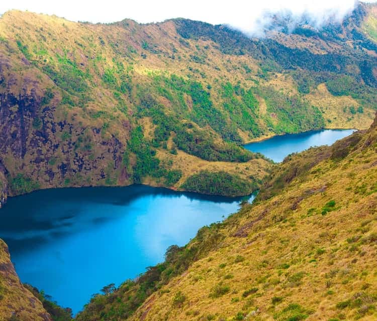 Aerial view of twin turquoise crater lakes nestled within steep, grassy mountain terrain, likely near Mount Wilhelm.