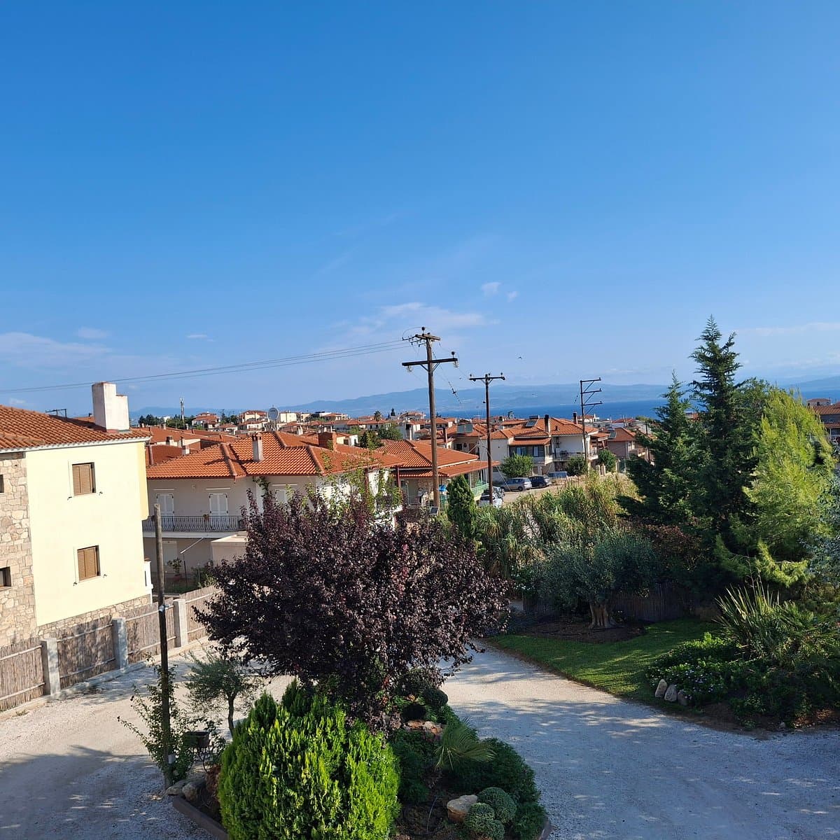 Sunlit view of a hillside village in Áfytos with terracotta roofs, overlooking the distant coastline and blue sea under a clear sky.