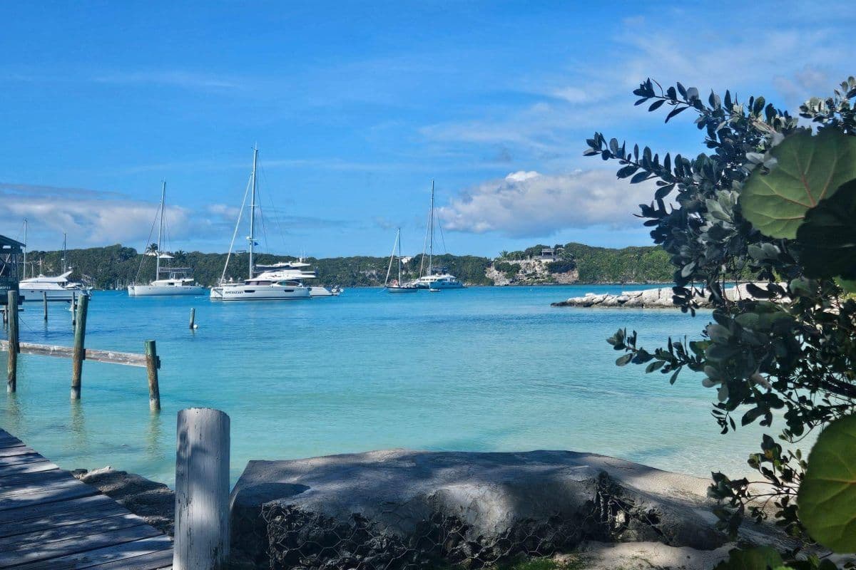 A scenic coastal view featuring turquoise waters, anchored sailboats, and a wooden dock, representing a transfer to Cooper's Town.