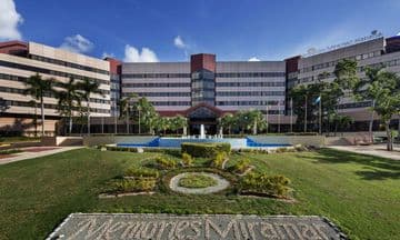 Exterior view of the Memories Miramar hotel complex featuring a large building, manicured lawns, a fountain, and a stone sign.