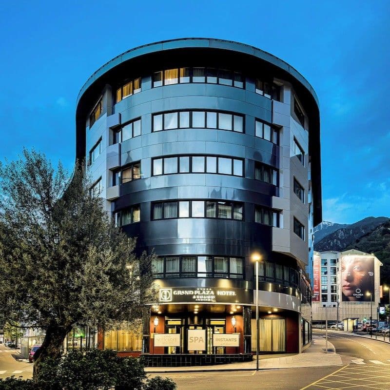 Exterior of the Grand Plaza Hotel in Les Escaldes at dusk, with mountains in the background.