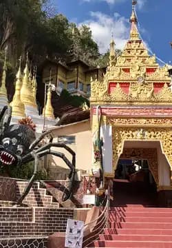 Exterior view of a golden temple complex in Pyapon featuring a large black spider sculpture near the entrance stairs.