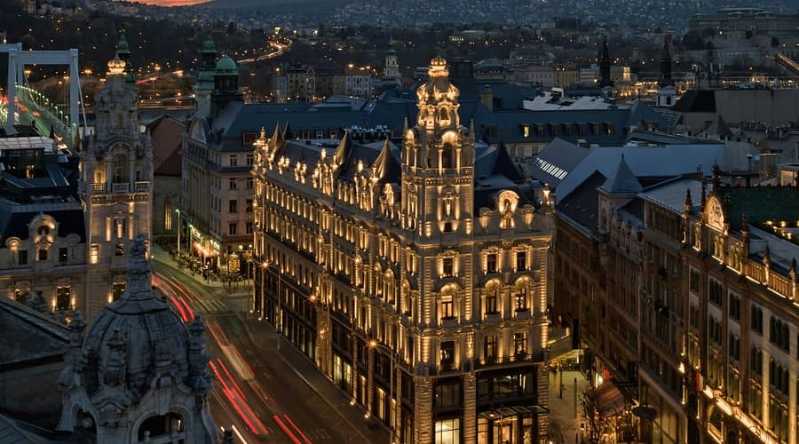 Illuminated historic architecture in Budapest at dusk, featuring the Grand Hotel Budapest and the Chain Bridge in the background.