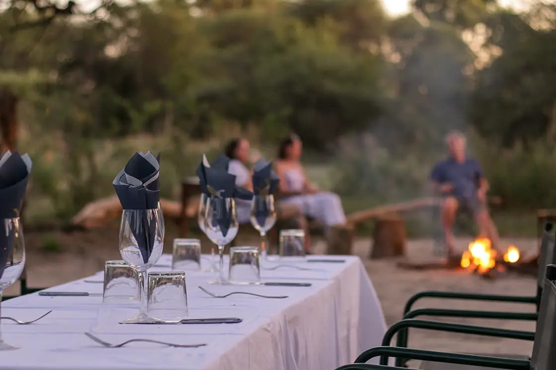 Set dining table with wine glasses on a wooden deck overlooking the bush landscape at dusk in Botswana