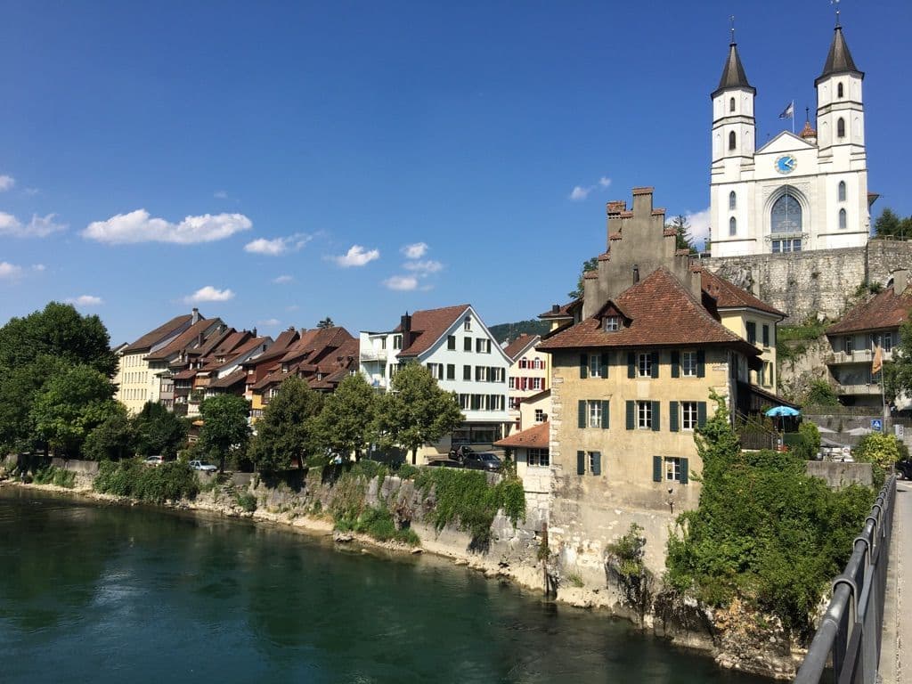 Riverside village street with traditional houses and a prominent twin-towered church near Wolfwil, Canton Solothurn.