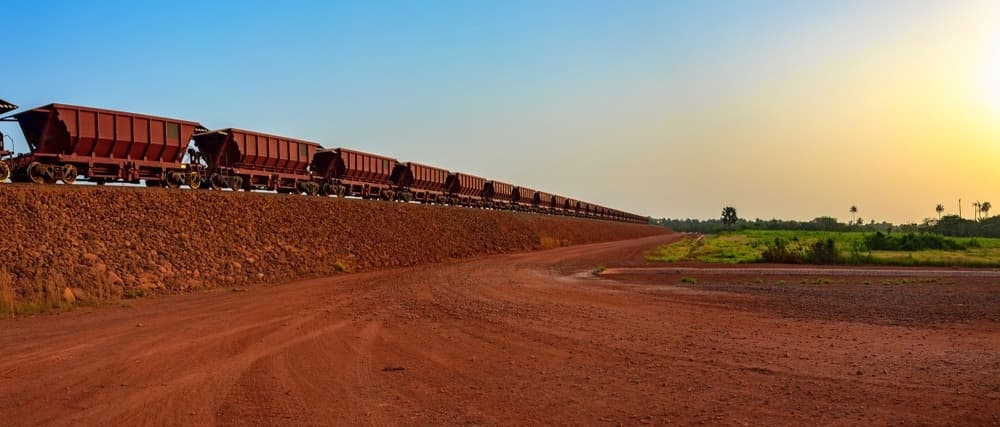 Freight train traversing a rocky embankment in a red-earth mining landscape in Guinea