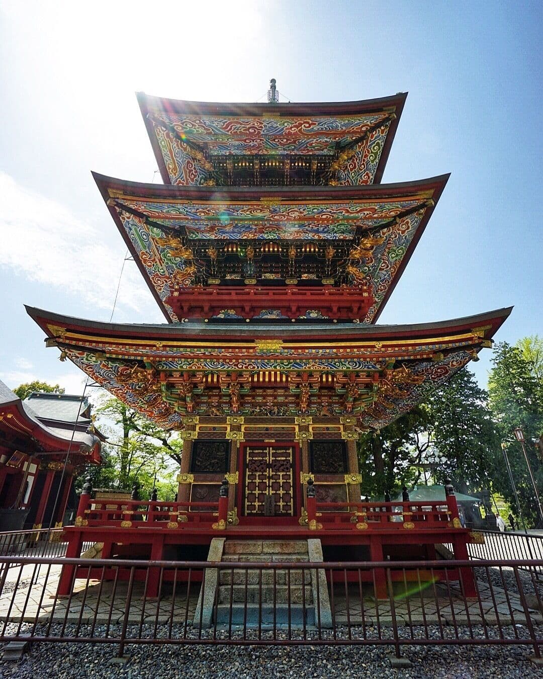 Low-angle view of a vibrant, three-story traditional Japanese pagoda with intricate colorful roof details and red pillars under a bright blue sky.