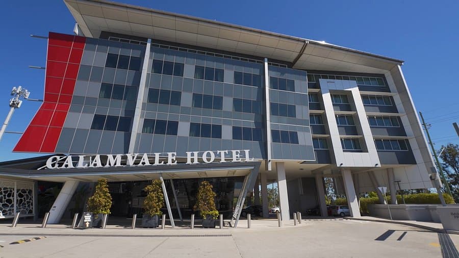 Exterior view of the Calamvale Hotel building featuring a modern facade with red accents and a clear blue sky.