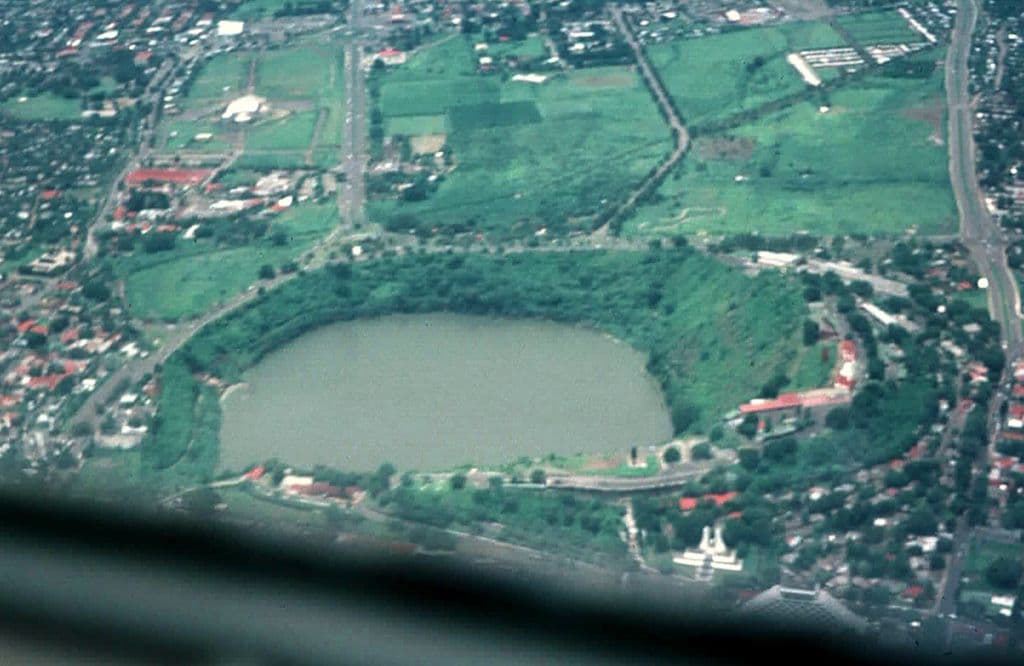 Aerial view of the Telica volcanic crater lake surrounded by green vegetation and nearby residential areas.