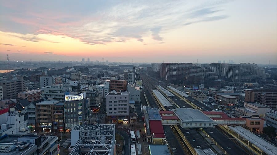 Aerial view of Abiko cityscape at dusk, featuring a railway station, urban buildings, and a colorful sunset sky.