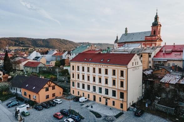 Aerial view of Kostelec na Hané town center featuring a prominent hotel building, a historic church with a tall tower, and surrounding residential architecture.