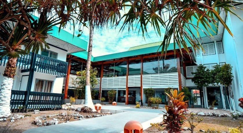 Exterior of a modern two-story guesthouse with teal roof, glass facade, and tropical landscaping.