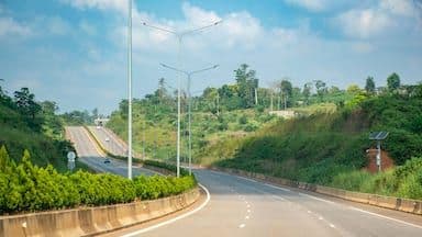A paved highway curves through a lush, green hilly landscape in coastal Cameroon, with streetlights and a concrete median