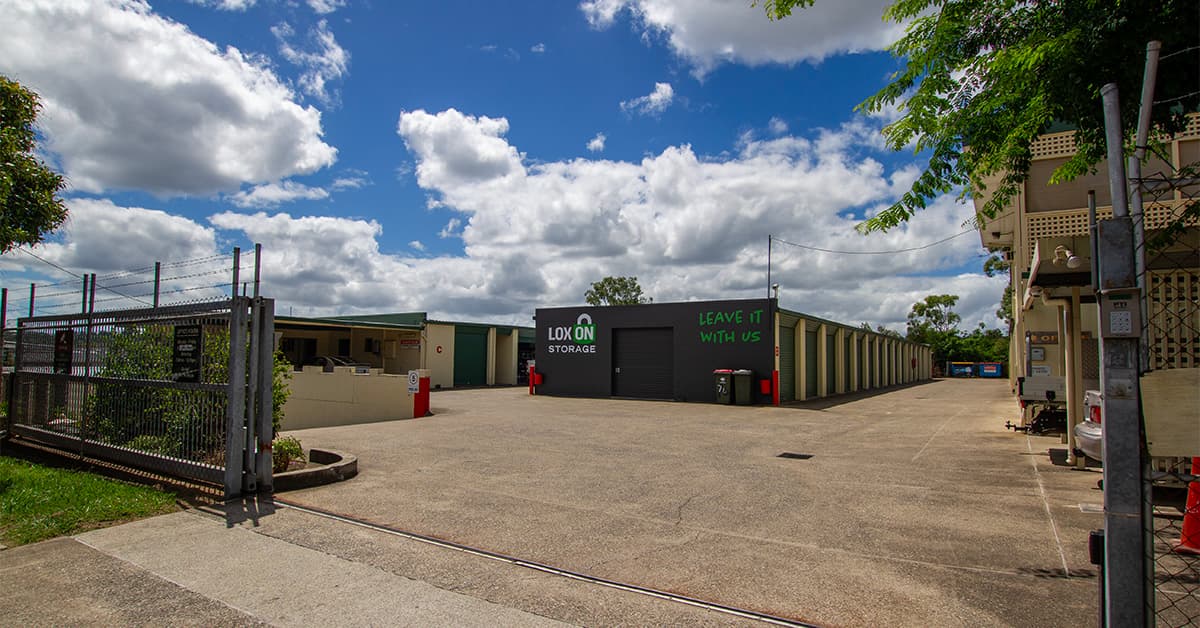Exterior view of Loxon Storage facility in Calamvale featuring industrial warehouse units, a paved driveway, and a bright blue sky with clouds.