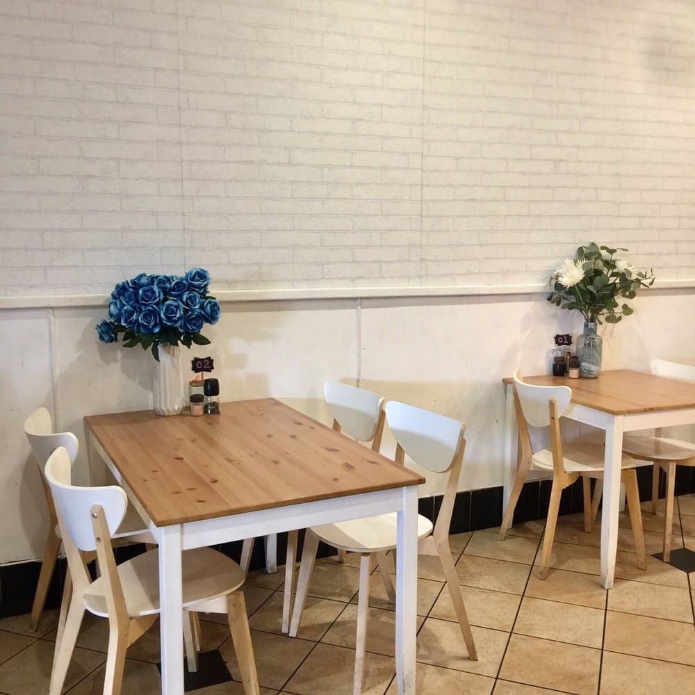 Interior view of a cafe featuring wooden tables, white chairs, and blue floral arrangements against a white brick wall.