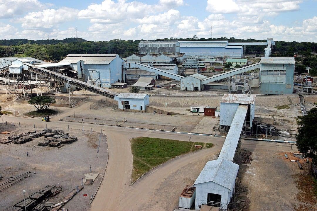 Aerial view of an industrial mining complex with conveyor belts, processing buildings, and dirt roads under a partly cloudy sky in the Chililabombwe, Zambia are