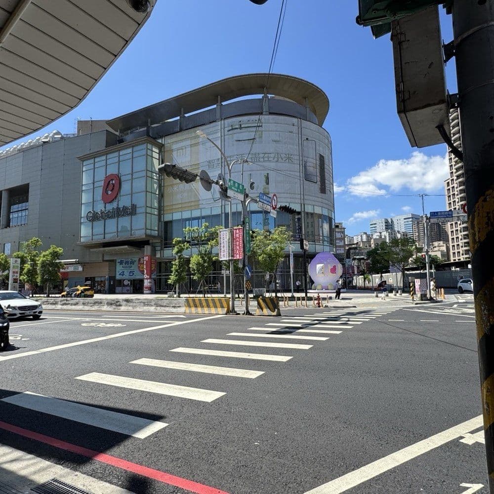 Street-level view of a Banqiao intersection featuring a crosswalk, traffic signals, and the CitiMall building under a clear blue sky.