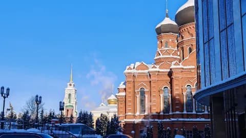 Snow-covered red brick church with onion domes and a white bell tower in a Russian town under a clear blue sky, illustrating late-autumn conditions in the Tula
