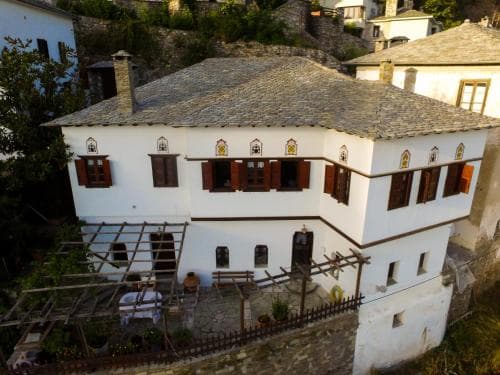 A white traditional Greek building in Áfytos with a stone roof and wooden shutters, featuring a small outdoor patio area with a table and pergola.