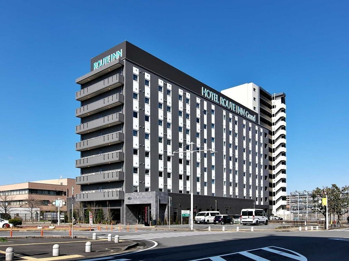 Exterior view of the Hotel Route-Inn Grand building under a clear blue sky, showing the modern facade and street-level entrance.