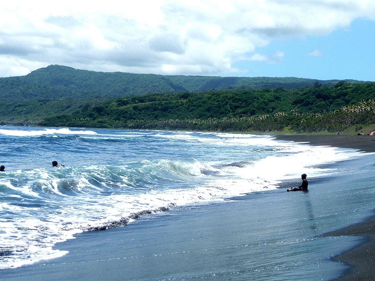 Black sand beach with clear blue water, breaking waves, and lush green hills at Louniel Beach, Tanna Island, Vanuatu