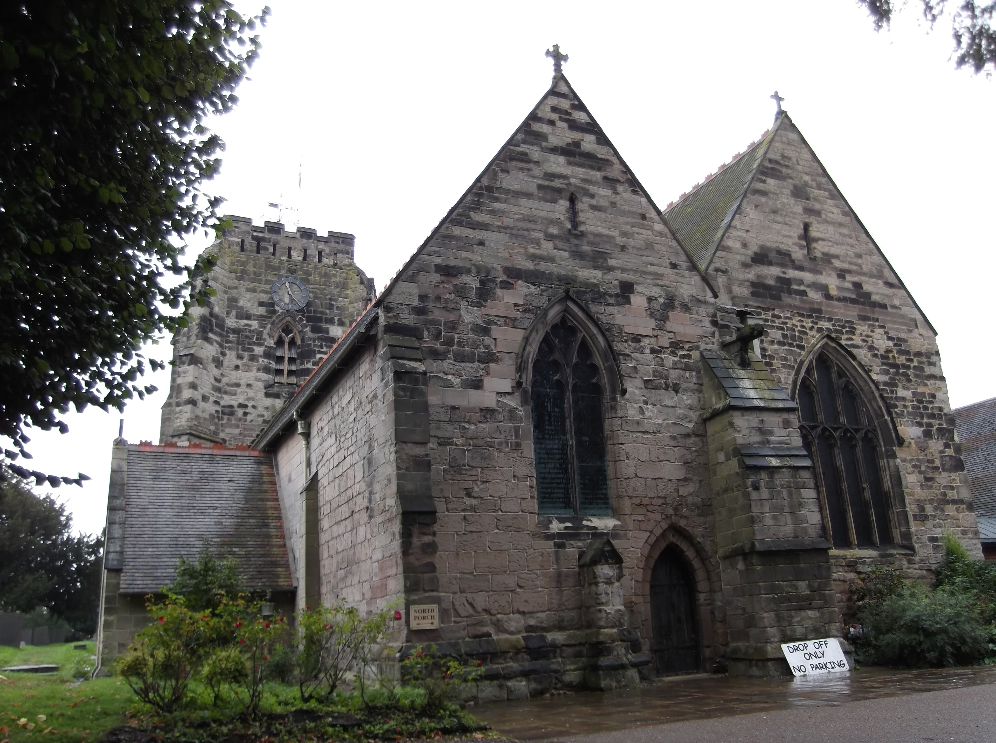 A stone church with a clock tower and Gothic windows stands under an overcast sky, featuring a 'North Porch' sign and a 'Drop Off Only' notice.