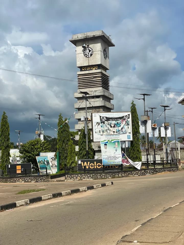 Exterior of the Bo Clock Tower in Sierra Leone, a concrete landmark with surrounding trees, banners, and an adjacent road.