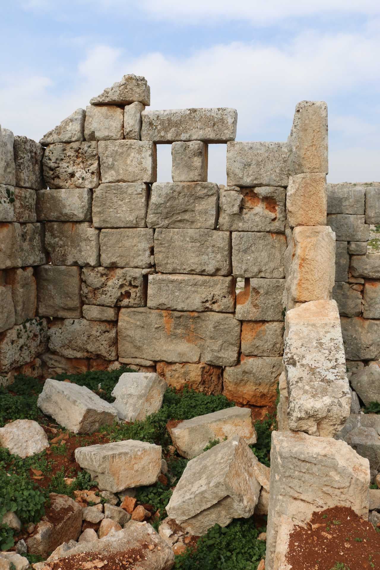 Close-up view of weathered stone masonry from a castle ruin, showing stacked blocks and scattered rubble against a cloudy sky.