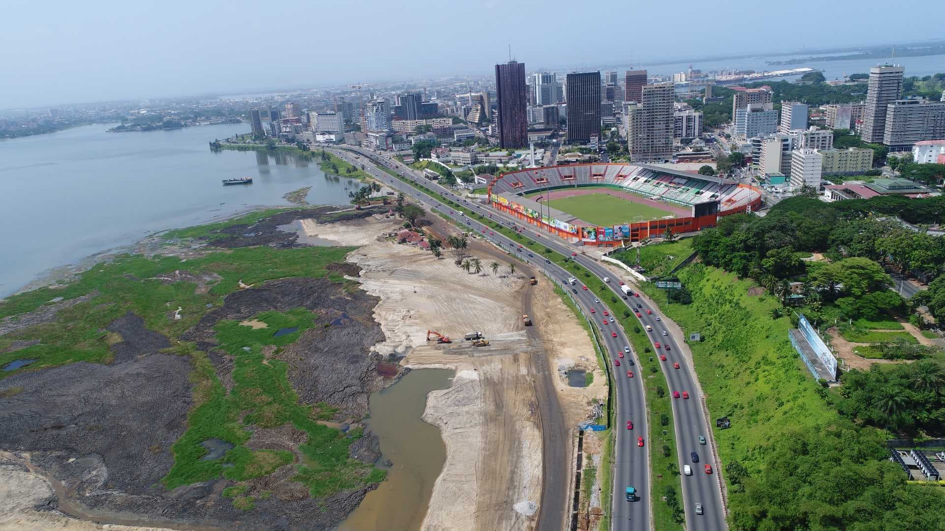 Aerial view of a coastal city with a multi-lane highway, stadium, waterfront, and construction site.