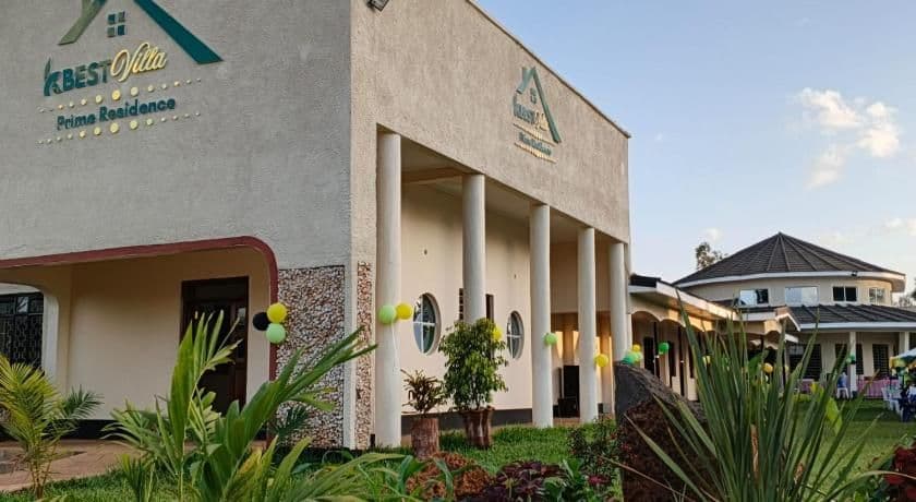 Exterior of a guesthouse building in Chuka, Kenya, with signage, columns, and landscaped grounds under a clear sky.