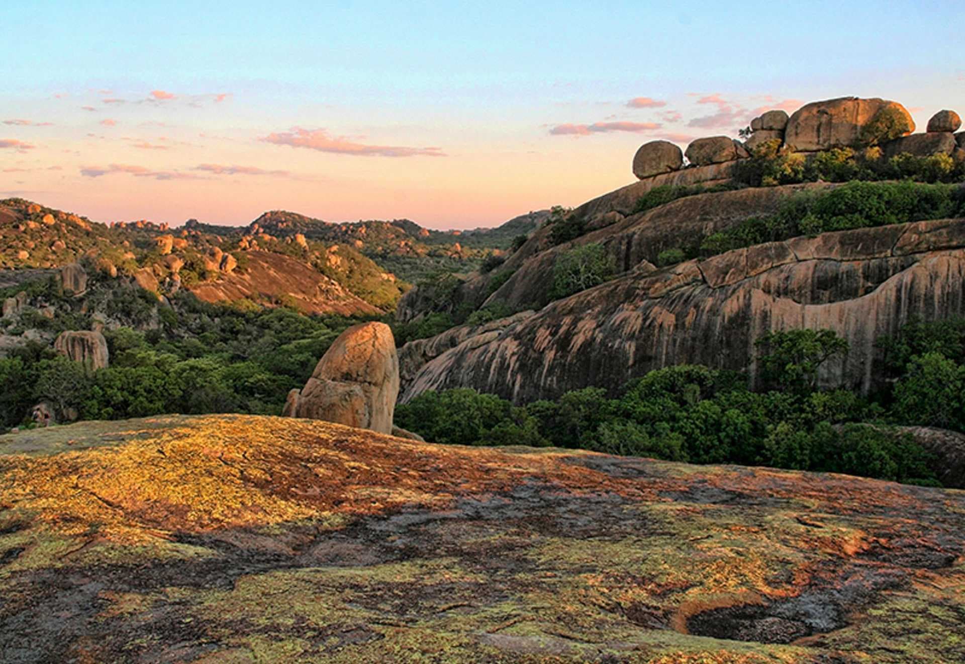 Granite boulders and rugged mountain terrain with green vegetation under a sunset sky in the Chimanimani area.