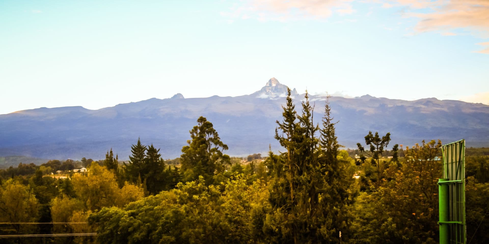 Wide landscape photograph of forested slopes and a distant Mount Kenya peak under a clear sky, viewed toward the slopes near Chuka, Kenya.