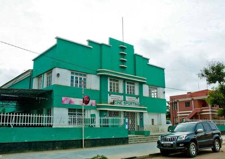 Green and white building labeled Cine Sporting, with a parked SUV and street scene.