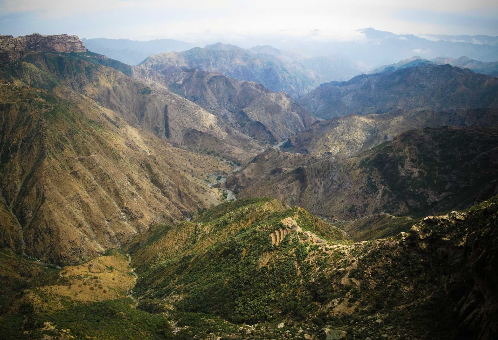 Highland mountain ridge and deep valley landscape near Adi Keyh, Eritrea, with layered peaks, sparse vegetation, and a winding river under a hazy sky.