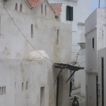 Narrow street scene with whitewashed earthen buildings, small windows, and a distant minaret in Smala.
